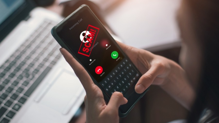 Person using a mobile phone with the word SCAM across the screen.