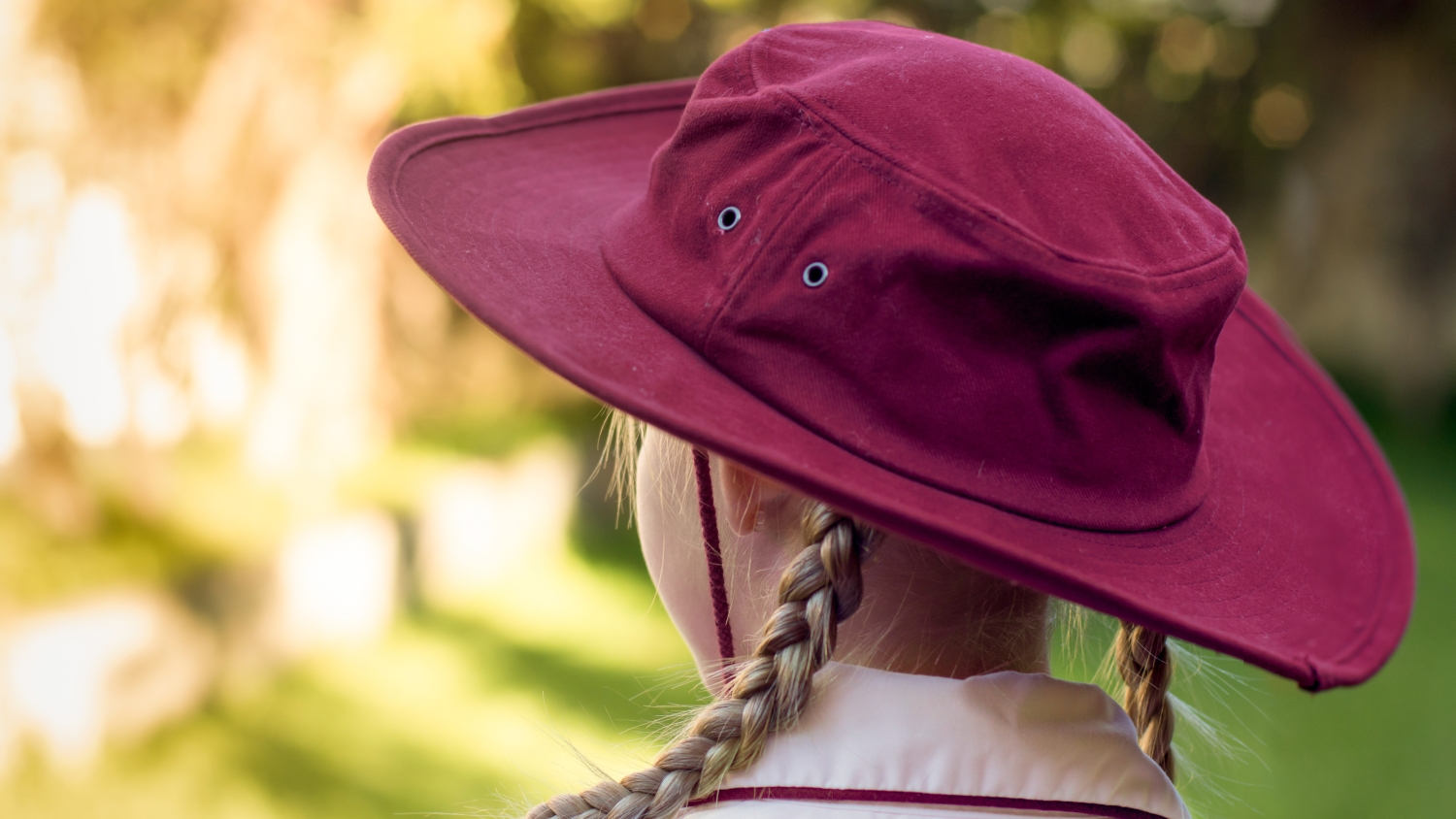 A close up of the back of the head of a primary school girl who is wearing a wide-brimmed hat.
