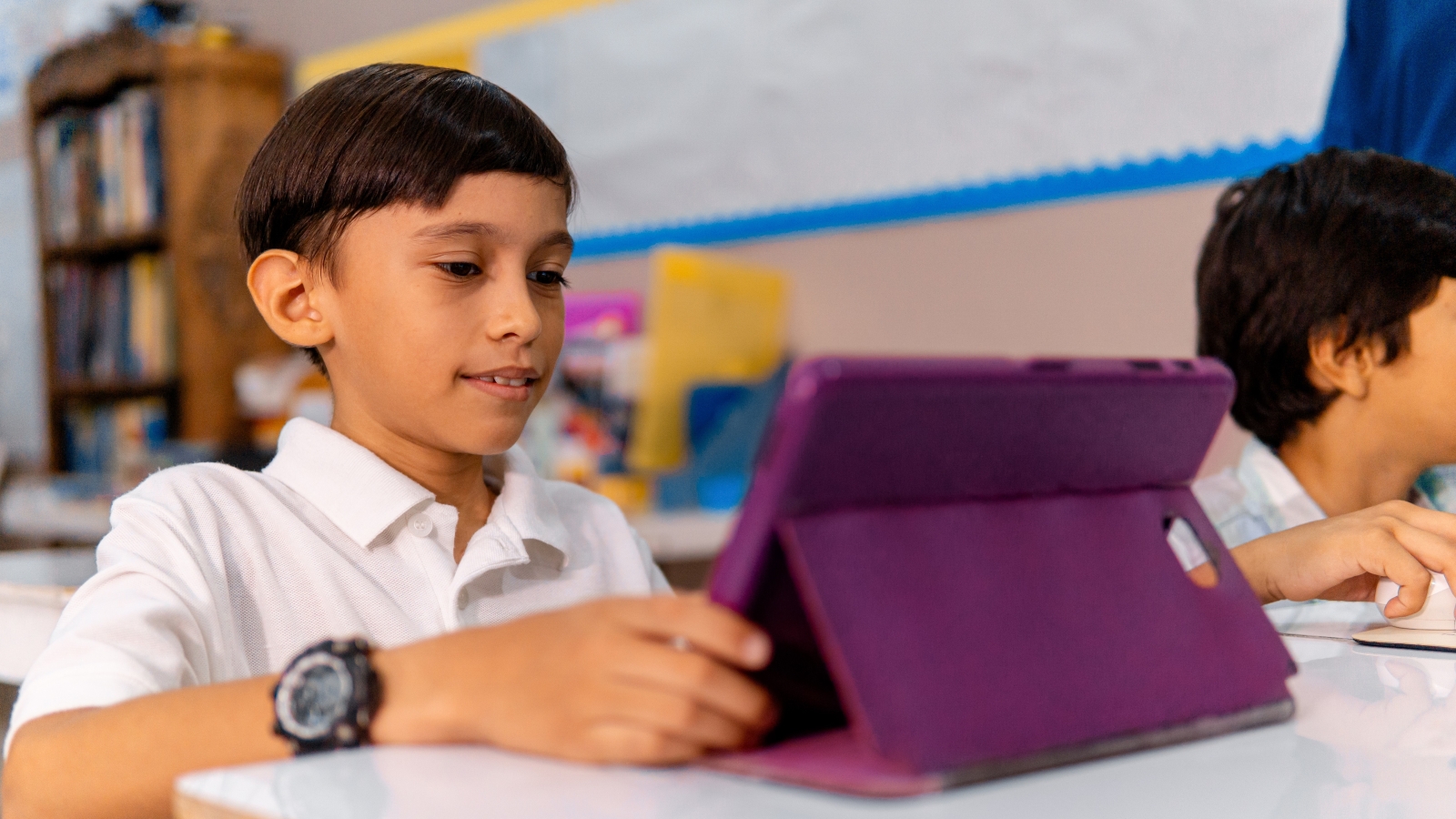 A close up of a primary school student sitting in a classroom and using a tablet.