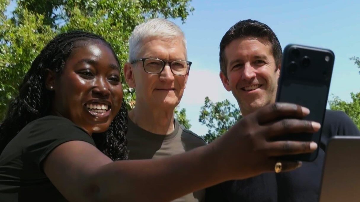 A close up of a woman using an iPhone to take a selfie with Tim Cook and John Ternus.