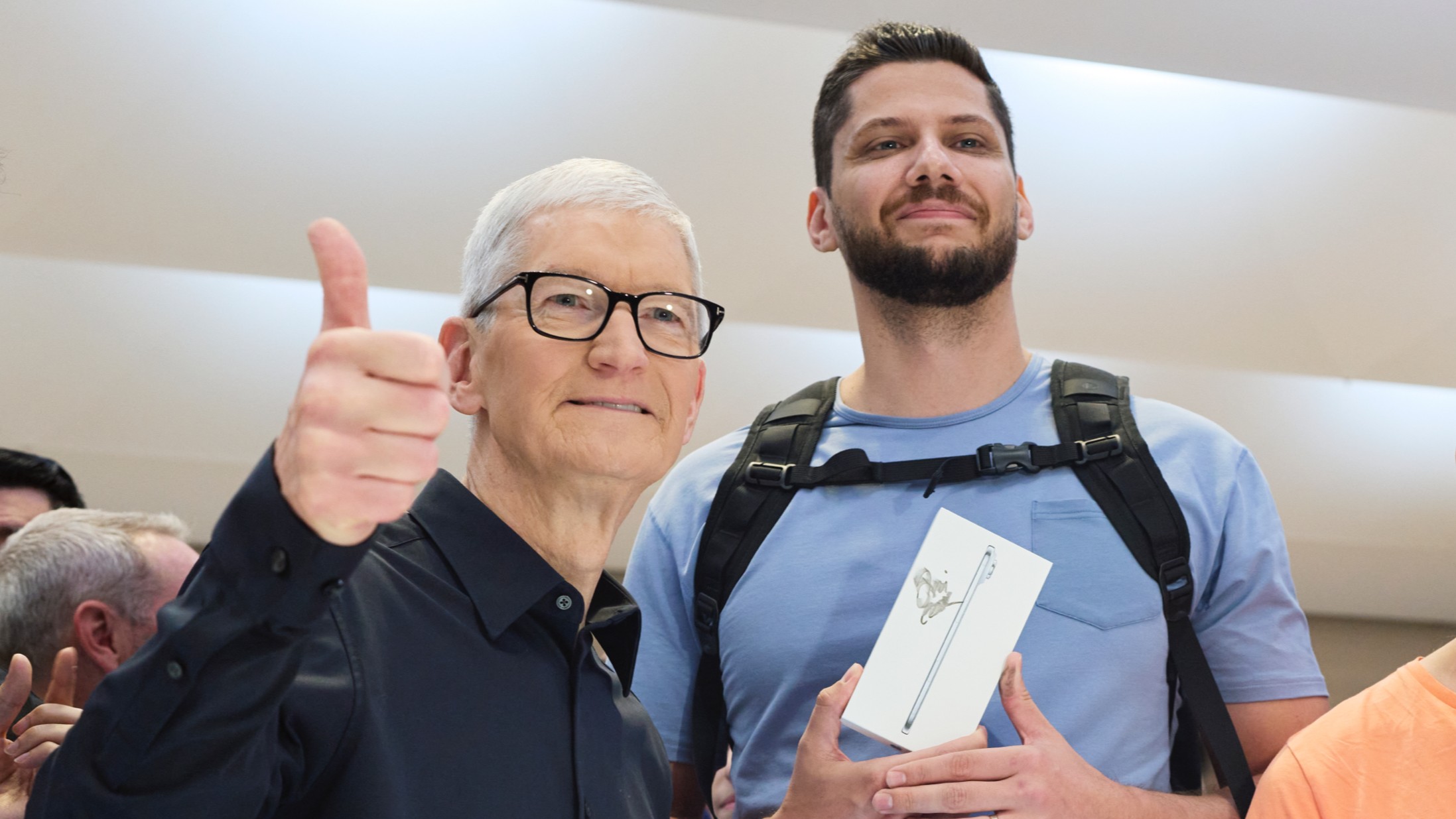 A close up of Tim Cook smiling and giving a thumbs up, standing next to a customer holding an iPhone Air box.