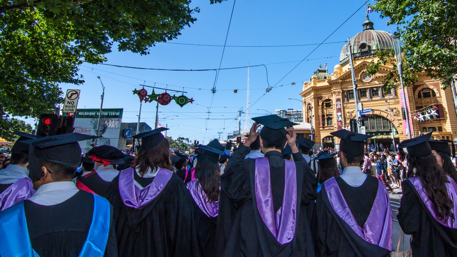 A medium shot of graduating university students in graduation gowns and hats walking through Melbourne's CBD.