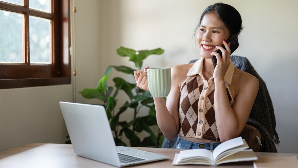Woman working from home, sitting at a laptop, holding a cup of coffee.