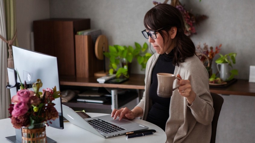 Woman working at laptop from home, holding a mug.
