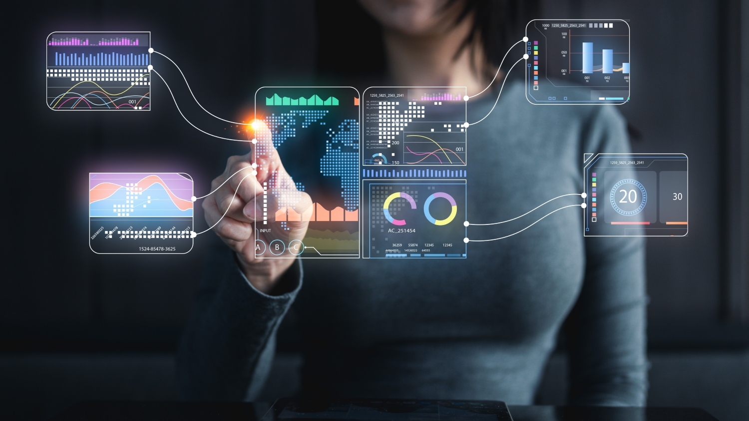 A close up of a woman sitting and using her index finger to point at data on a floating futuristic display in front of her.