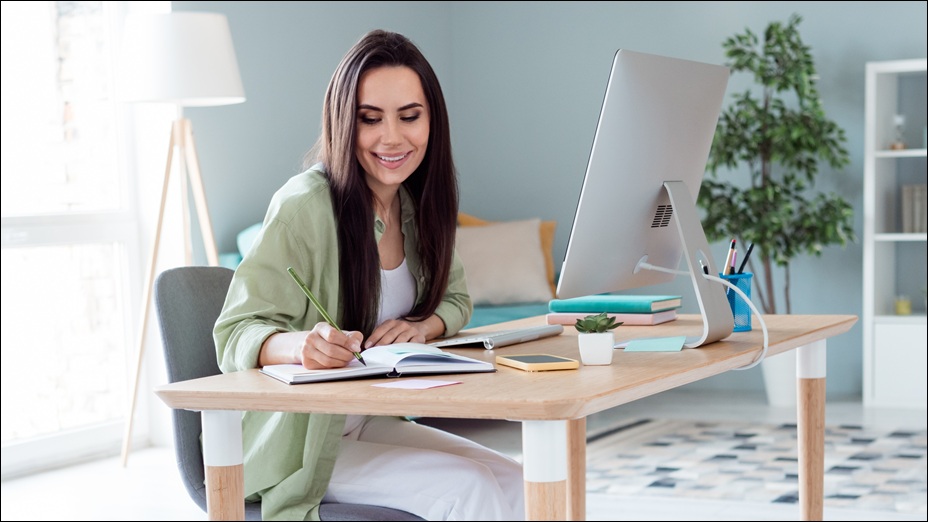 Woman working from home, sitting at a desk, smiling.